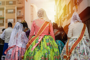 A group of Falleras women with colorful dresses and hair bun standing on a Valencia street, viewed...