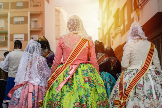 A group of Falleras women with colorful dresses and hair bun standing on a Valencia street, viewed from behind