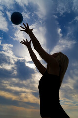 A young woman exercising with a ball shot on a beach in silhouette against a dramatic early morning sky