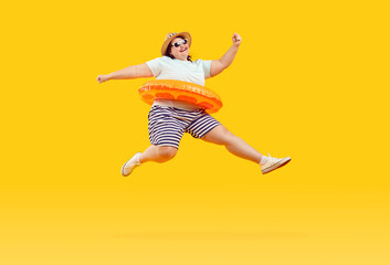 Fototapeta na wymiar Full body photo of a happy funny fat plus size overweight woman in sunglasses with rubber ring jumping and having fun on studio yellow background. Summer holiday trip and vacation concept.