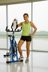 Fototapeta premium Mid adult Asian woman standing with exercise bicycle smiling at viewer.