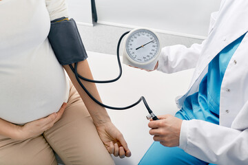 Doctor measuring blood pressure of pregnant woman on maternity leave while visit by perinatal center. Examinations during pregnancy - obrazy, fototapety, plakaty
