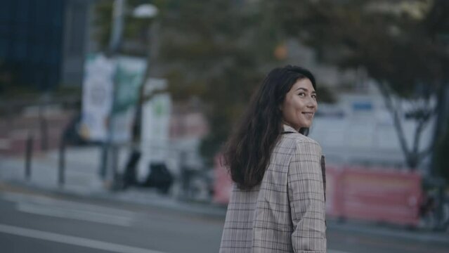 Portrait of businesslady crossing street. Young woman in business district with skyscrapers, heading to job. During the scene, girl turn head and smiling to camera. Concept of work, lifestyle.