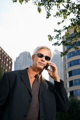 Caucasian middle aged businessman in sunglasses talking outdoors on cell phone.