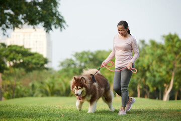 Joyful Asian woman walking in city park with samoyed dog