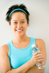 Young woman in exercise clothes holding bottle of water smiling.