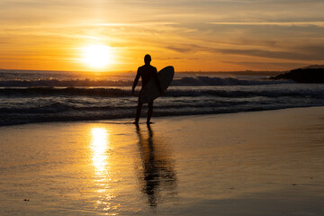 Silhouette of a lonely man surfer holding surfboard on the seashore