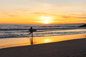 A man surfer running on the seashore at sunset