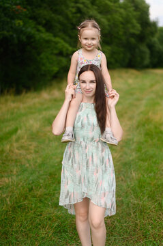 Mom and girl spend time together outdoors. The mother holds her daughter on her neck. Mother day, baby day