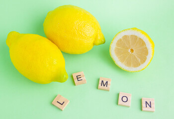 Limones frescos sobre un fondo verde y unas letras de madera con la palabra limón