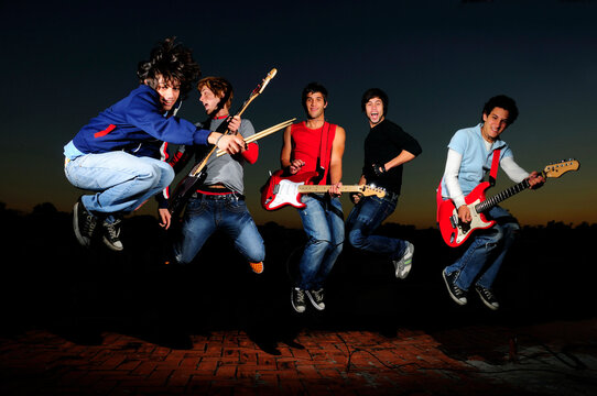 Portrait of young trendy teenager group jumping with musical instruments
