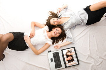 Two Young girls relax with laptop lying on the floor