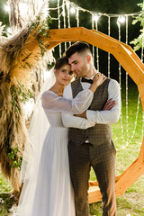 happy couple of newlyweds at night near the wooden wedding arch. grainy and slightly blurry effect. wedding couple at the ceremony. christian couple. rustic wedding decor