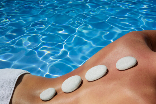Woman with volcanic massage stones in front of a blue spa pool