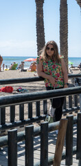 Mujer caucásica rubia, con gafas de sol, apoyada sobre un puente cerca de la playa en el sur de España
