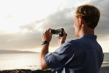 Smiling Caucasian man photographing a scenic sunset at a beach. Horizontal format.
