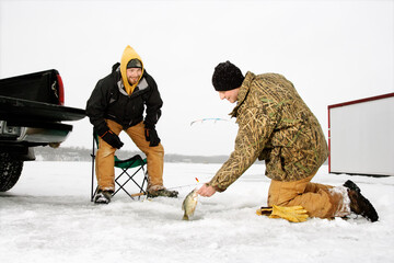 Fototapeta na wymiar Two young men ice fishing in a winter environment. Horizontal shot.