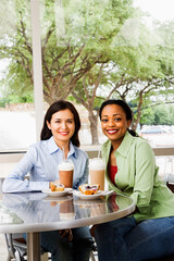 Two smiling woman sitting enjoying muffins and coffee drinks at a cafe. Vertical shot.