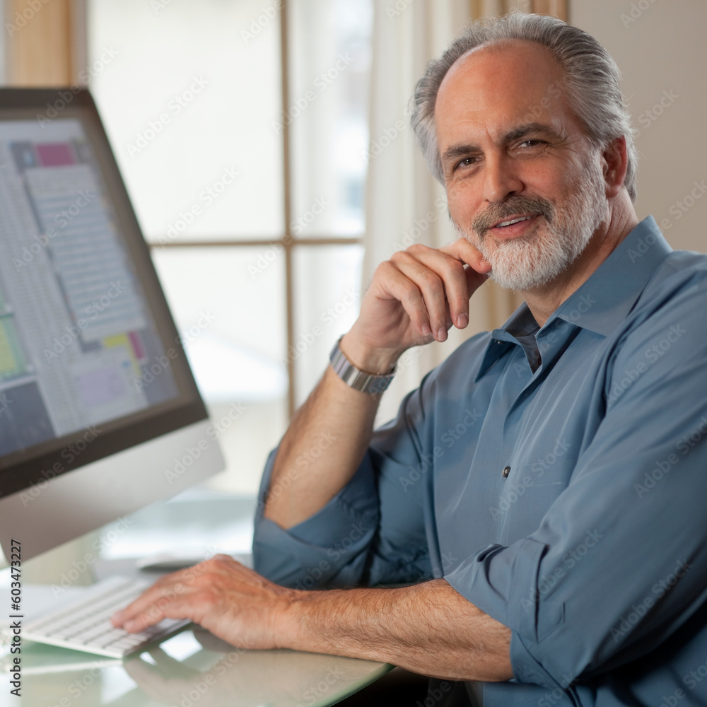 Poster portrait of a businessman dressed in casual clothing and sitting in front of a computer. he is smili