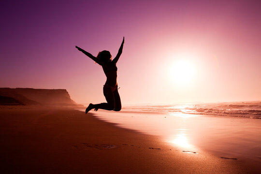 Picture of a female silhouette of a young girl jumping on the beach at the sunset