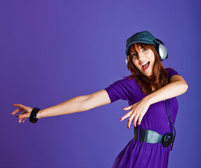 Beautiful and happy young woman listen music with headphones, over a violet background