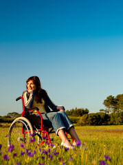 Happy handicapped woman on a wheelchair over a green meadow
