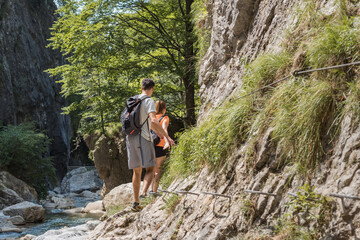Young couple hiking along the rocky shore of a mountain river, exploring beautiful nature. Concept of an active vacation.
