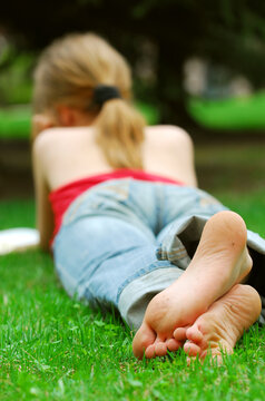 Young girl relaxing with a book on green grass in a summer park