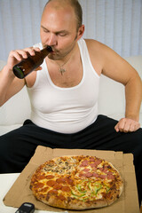 Unhealthy fat man sitting on the couch with beer and pizza
