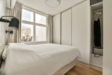 a bedroom with a bed and closets in the back ground, there is a large window that looks out onto the street