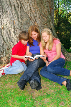 Portrait of a family - mother and children - reading a book in a park