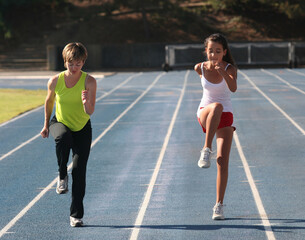 Fototapeta premium Mother and daughter exercising on a blue racetrack