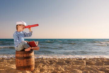 Happy child sitting on old barrel against sea and sky. Summer vacation and travel concept - obrazy, fototapety, plakaty