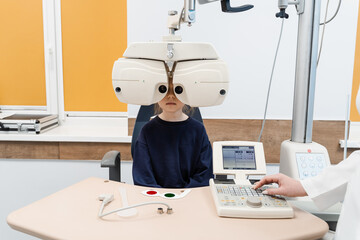 Child looks into phoropter during an eye examination of pediatric ophthalmologist. Phoropter for...