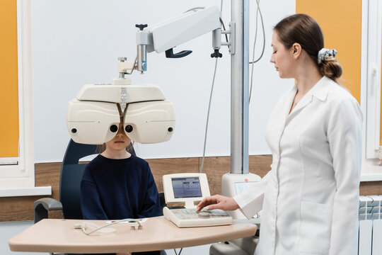 Child looks into phoropter during an eye examination of pediatric ophthalmologist. Phoropter for measuring refractive error and determining information for prescription for eyeglasses.