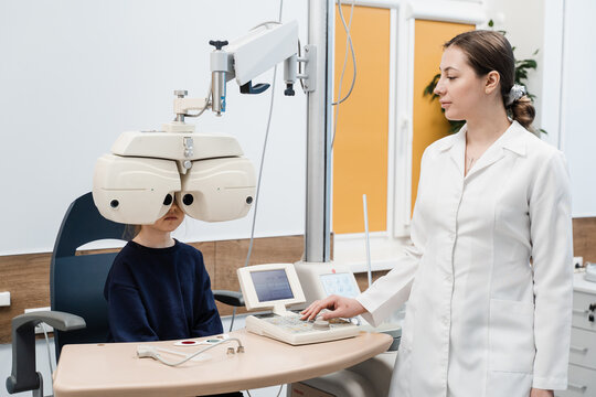 Child looks into phoropter during an eye examination of pediatric ophthalmologist. Phoropter for measuring refractive error and determining information for prescription for eyeglasses.