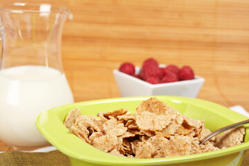 A bowl of cornflakes, milk and raspberries on bamboo mat. Shallow depth of field