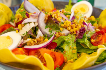 Mixted salad with vegetarian dumplings, boiled eggs, green leaves , tomatoes, onion on a wooden big plate