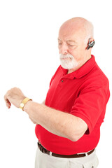 Senior man talking on his hands free set checks his watch.  Isolated on white.