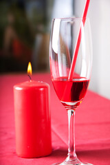Red cocktail in a glass with a straw and a red candle