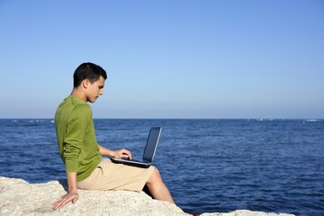 Handsome young businessman with computer on the blue ocean beach