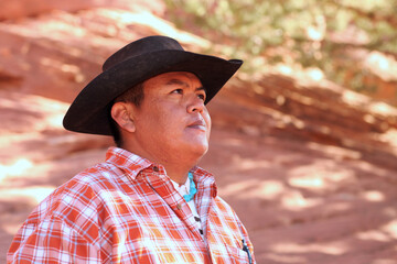Mid adult male wearing cowboy hat. He is head and shoulders viewable and looking away from the camera. Horizontally framed shot.