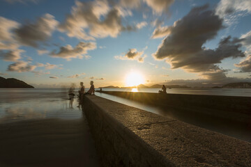 Santos city, Brazil. Sunset at the end of the beach. Water Channel Bridge nº6. People enjoying the beach on the short wall. Long exposure photography.