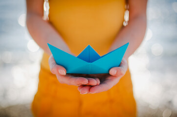 A woman's hand holding blue paper boat