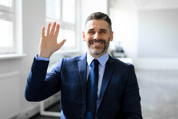 Fototapeta premium Business communication employment. Successful middle aged businessman waving hello and smiling to camera