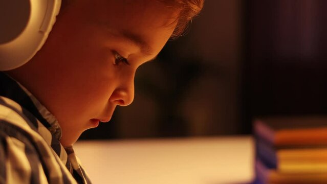 Cute boy student in headphones studying online from home, watching web lesson or listening to tutor via video call, e-learning on pandemic isolation. Distance education of children. Clouse up view.