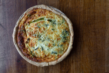 Quiche. Fresh eggs mixed with vegetables, bacon, ham, sausage, cheese, and Broccoli. The round shape on rustic wooden board.