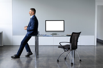 Successful businessman in formalwear sitting leaning on table with blank computer monitor mockup, copy space