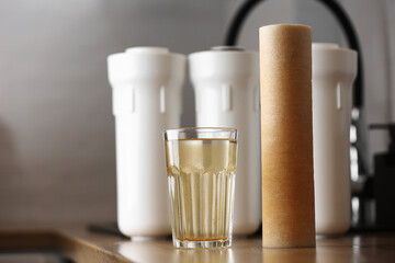 Water filter cartridge used and a glass of rusty water brown coloring on wooden table at kitchen interior. Plastic set with three filter cartridges reverse osmosis water purification system.
