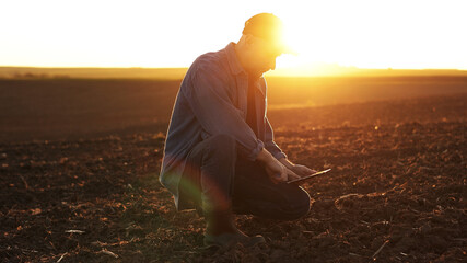 Agronomist touches soil examine and testing cultivated land before sowing on agricultural field and typing results in digital tablet on sunset. Smart farming technology and organic agriculture. © Andriy Medvediuk